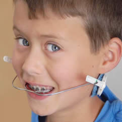 Young boy with blue eyes and blue shirt wearing headgear.